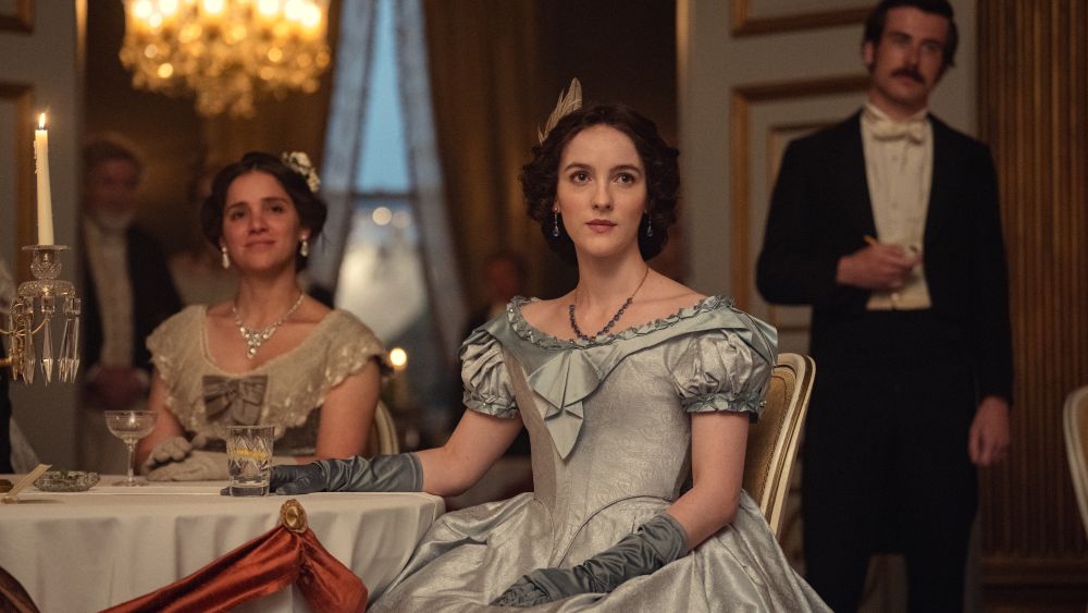 Adelaide sitting at a table in a formal dress.