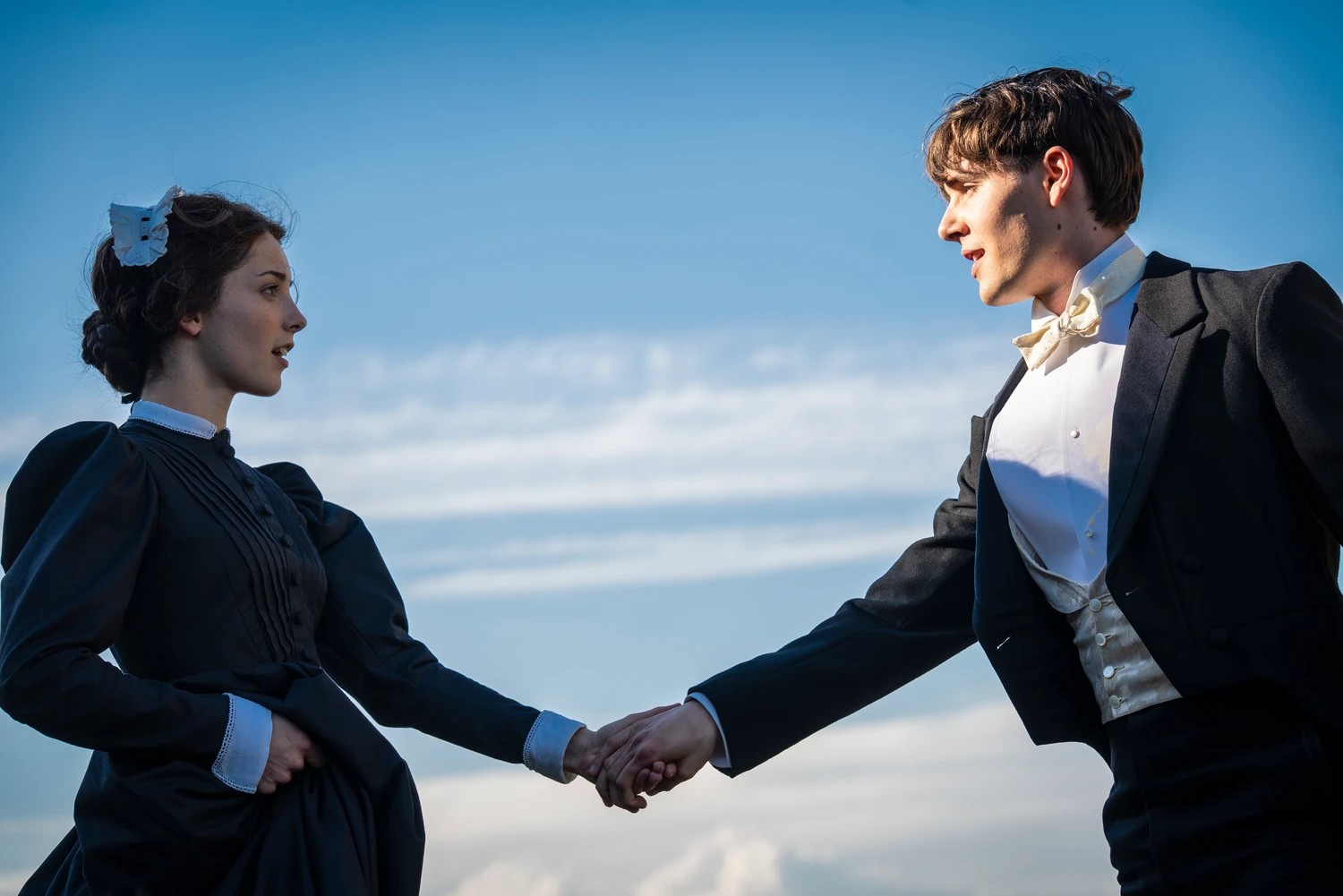 A young woman and man standing apart but holding hands