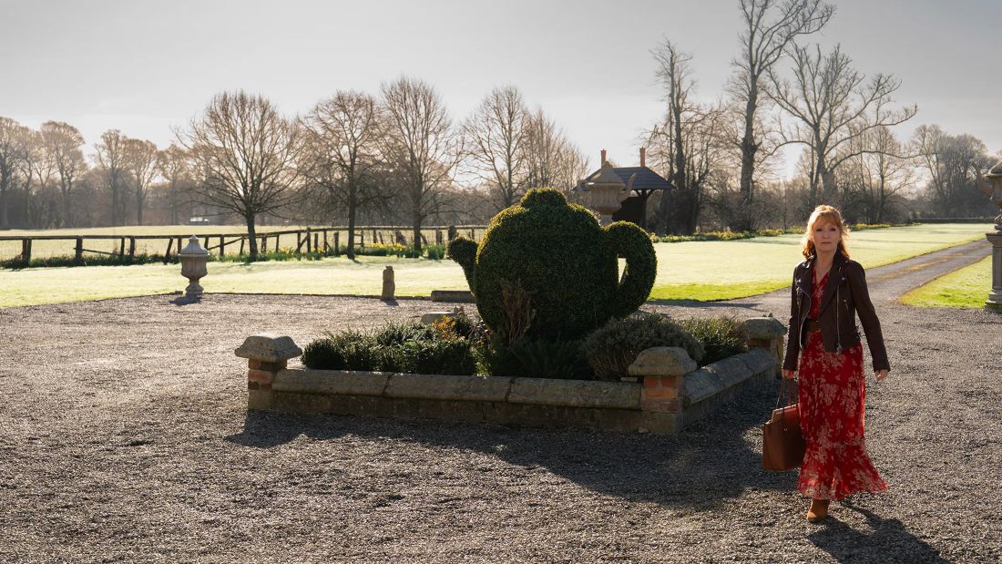 Susan walking in a beautiful garden outside a manor house