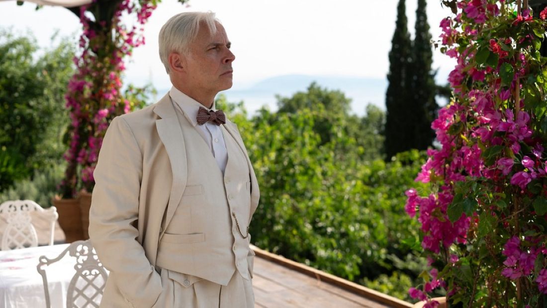 Man with grey hair in a dapper beige suit in a garden