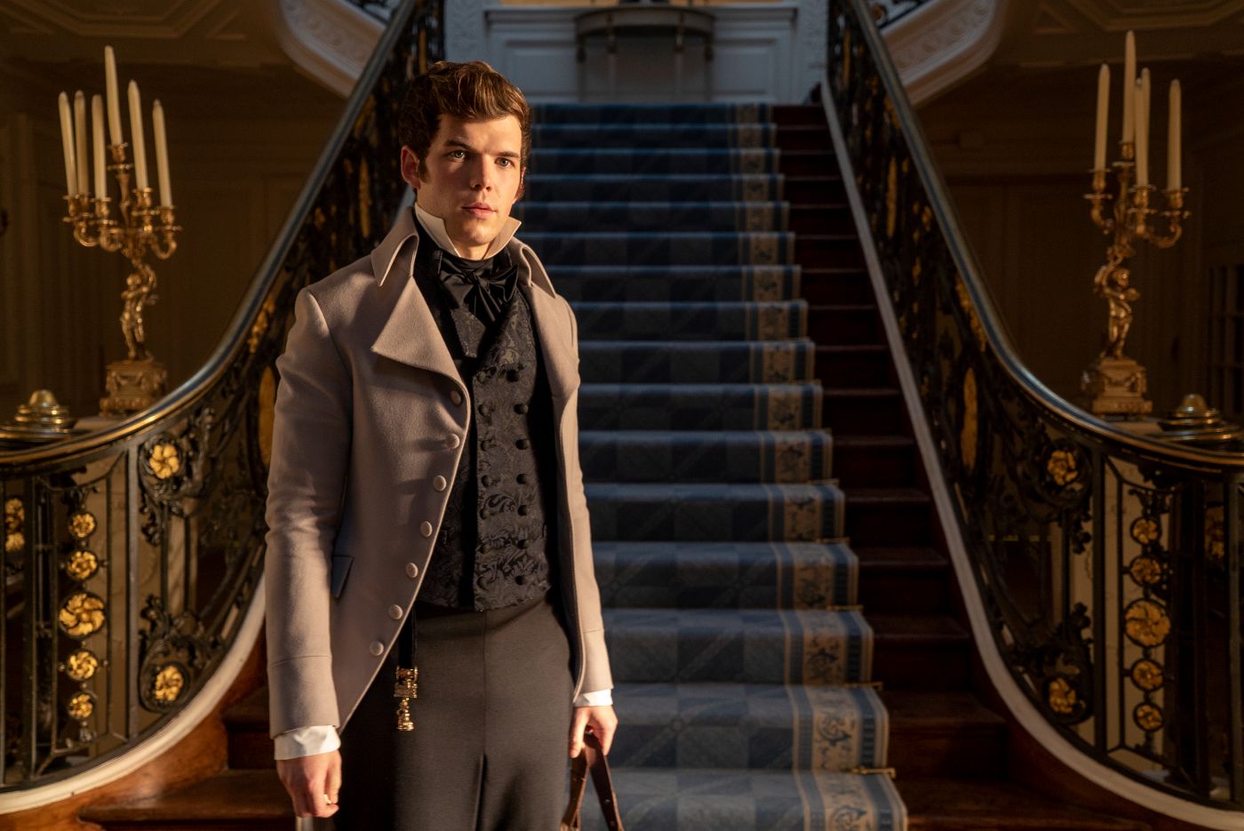 Colin Bridgerton stands at the foot of a grand staircase in Bridgerton Season 1 Episode 6.