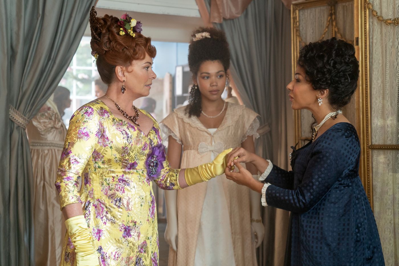 Lady Featherington speaks with Lady Danbury as Marina Thompson stands behind them in Bridgerton Season 1 Episode 6.