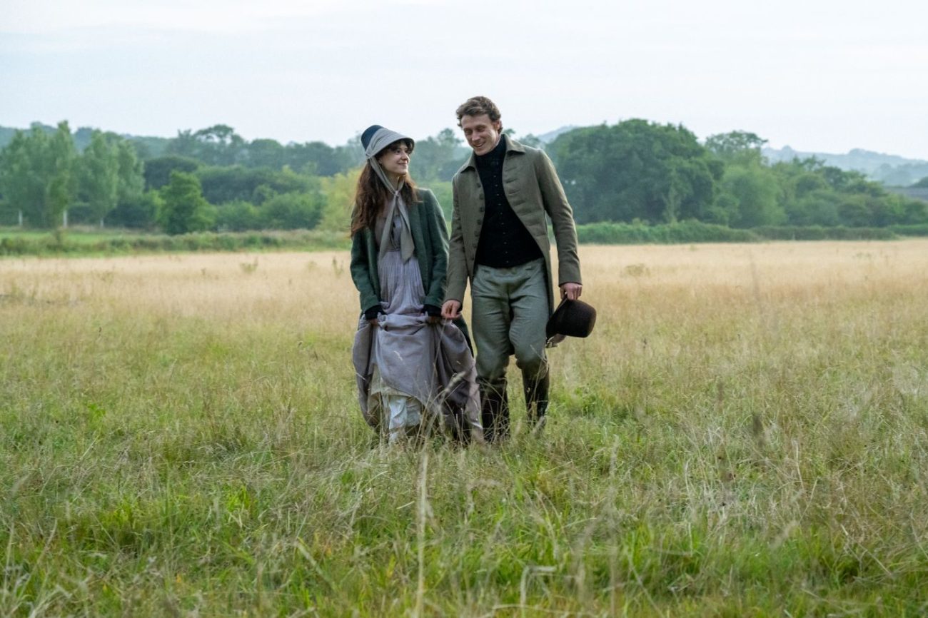 Daisy Edgar-Jones as Elinor Dashwood and George MacKay as Edward Ferrars walking together through a field in Sense and Sensibility.